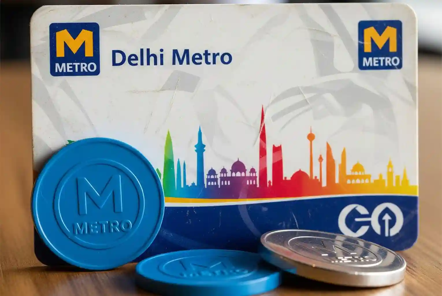A Delhi Metro smart card and several blue tokens on a wooden surface.